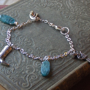 Puede incluir: Un brazalete de plata con piedras turquesa, un dije de bota vaquera, un dije de sombrero vaquero y un dije de pistola.