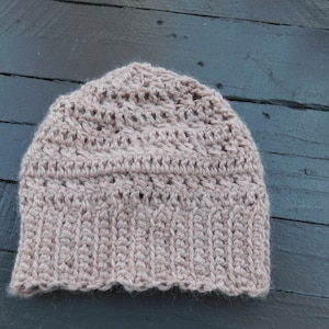 May include: A crocheted beanie in a light brown color. The beanie has a simple stitch pattern and a slightly slouchy fit.