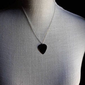 Peut inclure: Un collier en chaîne argent avec un pendentif en forme de médiator de guitare noir.