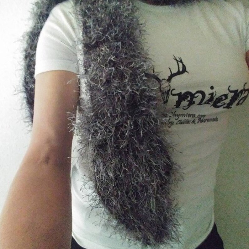 May include: A white t-shirt with a black deer head and the word "mier" printed on the front. The shirt is worn with a gray fluffy scarf.