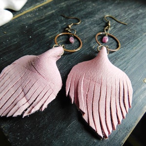 May include: A pair of pink leather fringe earrings with a small pink stone and a gold hoop.