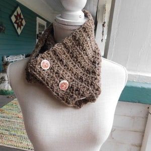 May include: A brown crocheted cowl with two decorative buttons. The cowl is displayed on a white mannequin.