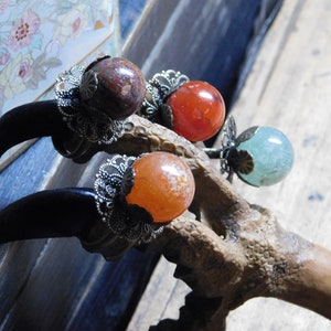 May include: Four rings with different colored stones set in claw-like metal bands. The stones are red, orange, green, and brown.