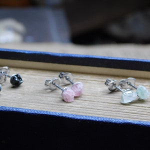 May include: Three pairs of earrings with different colored stones. The first pair has black stones, the second pair has pink stones, and the third pair has green stones.