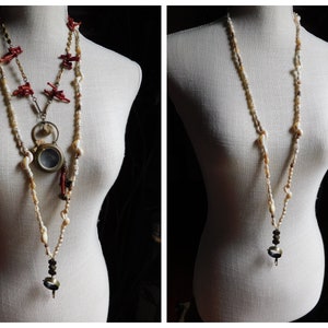 May include: Two necklaces on a white mannequin. The necklace on the left is made of red coral, gold chain, and white shell beads. The necklace on the right is made of white shell beads and has a small, round, silver pendant.