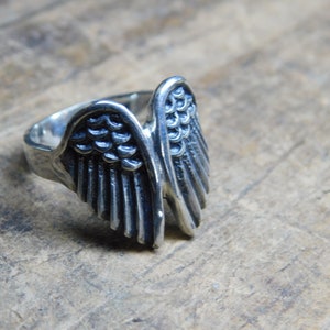 May include: A silver ring with a detailed wing design. The wings are spread out and have a textured surface.