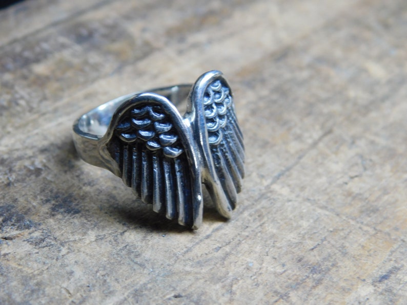 May include: A silver ring with a detailed wing design. The wings are spread out and have a textured surface.