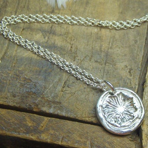May include: A silver necklace with a round pendant featuring a detailed floral design. The pendant is textured and has a raised center.