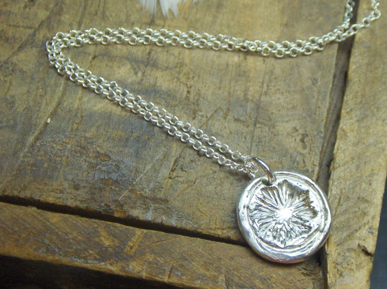 May include: A silver necklace with a round pendant featuring a detailed floral design. The pendant is textured and has a raised center.