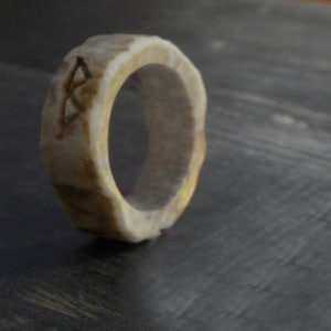 May include: A ring made from natural antler with a carved design. The ring is a light brown colour and has a smooth, polished finish.