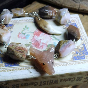 May include: A pink and brown agate stone bracelet with a wolf charm. The bracelet is made with wire and has a variety of different shaped stones.