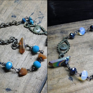 May include: Two sets of jewelry featuring a ring, chain, and various beads. The first set has a turquoise ring, a chain with a bronze eye charm, and beads in shades of orange and blue. The second set has a dark blue ring, a chain with a bronze eye charm, and beads in shades of black, white, and gray.