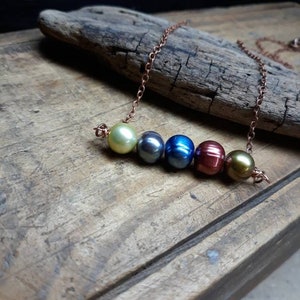 May include: A copper chain necklace with six iridescent pearls in shades of green, blue, and red.