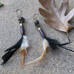 May include: A pair of long, dangling earrings with brown wooden beads, gold accents, and black and white feathers.