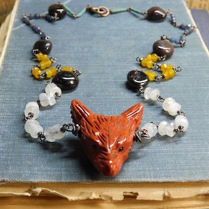 Può includere: Una collana con un ciondolo a forma di testa di volpe intagliata, perline di pietra di luna bianca, perline di citrino giallo e perline di pietre preziose blu scuro e nere.