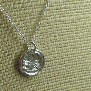 May include: A silver necklace with a round pendant featuring a textured, circular design. The pendant is attached to a delicate silver chain.