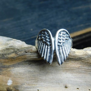 May include: A silver ring with a detailed wing design. The wings are spread out and have a textured surface.