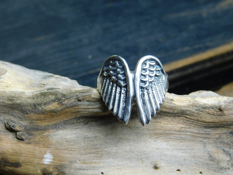 May include: A silver ring with a detailed wing design. The wings are spread out and have a textured surface.