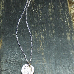 May include: A silver chain necklace with a round pendant featuring a detailed floral design.