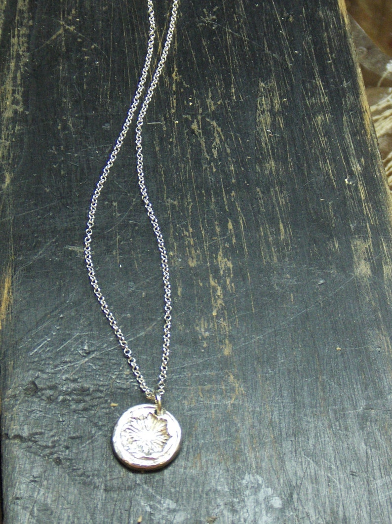 May include: A silver chain necklace with a round pendant featuring a detailed floral design.