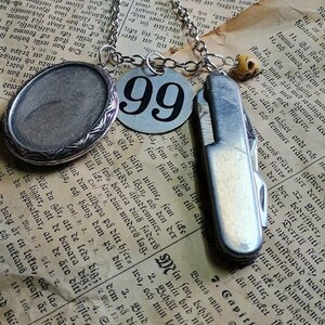 May include: A silver necklace with a pendant marked "99", a small pocket knife, and an oval locket. The items are displayed on a backdrop of aged book pages with text.