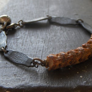 Può includere: Un braccialetto argento e nero con un ciondolo in osso marrone intagliato. Il braccialetto ha una chiusura ed è fatto di maglie di metallo.