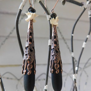 May include: A pair of black and copper earrings with a bone-shaped charm and a teardrop-shaped pendant.