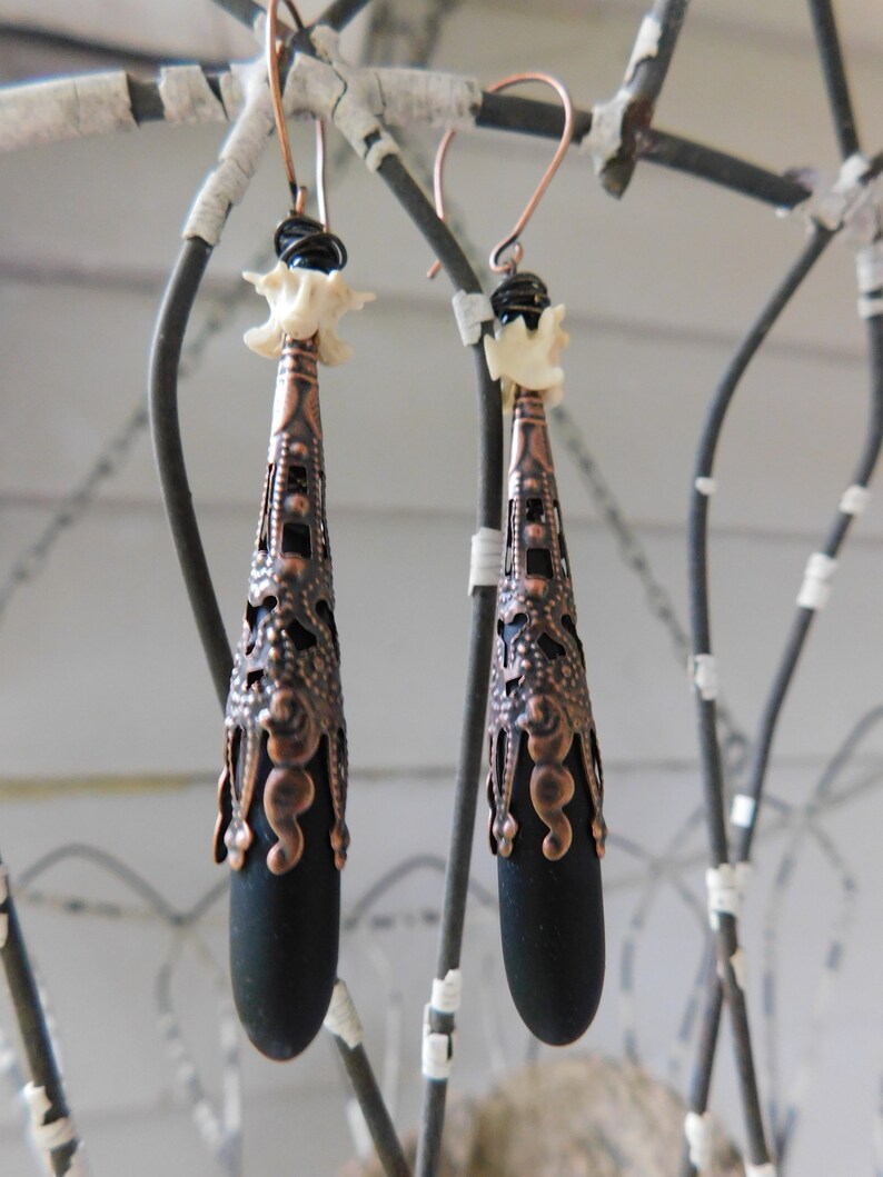 May include: A pair of black and copper earrings with a bone-shaped charm and a teardrop-shaped pendant.