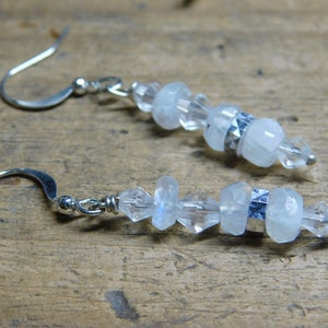 May include: A pair of silver earrings featuring white moonstone and clear crystal beads. The earrings have a silver hook fastening.