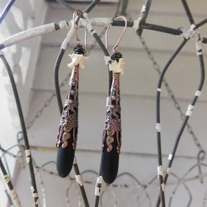 May include: A pair of dangle earrings with black teardrop-shaped beads, copper filigree accents, and white bone beads at the top.