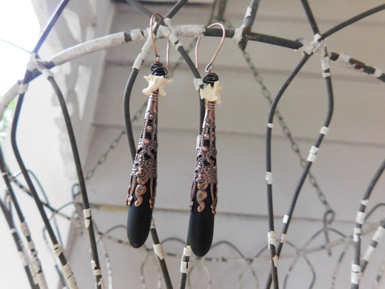 May include: A pair of dangle earrings with black teardrop-shaped beads, copper filigree accents, and white bone beads at the top.