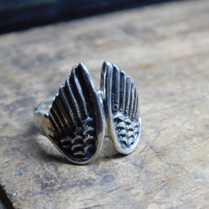 May include: A silver ring with a detailed design of two wings.