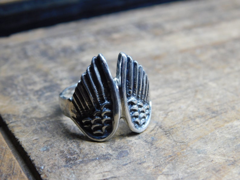 May include: A silver ring with a detailed design of two wings.