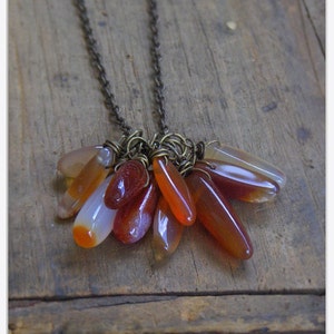 May include: A necklace with a cluster of teardrop-shaped carnelian stones in shades of orange, red, and white. The stones are attached to a brass chain with wire wraps.
