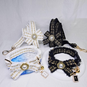 Puede incluir: Un conjunto de accesorios para mascotas, que incluye un transportín blanco y dorado, una correa negra y dorada y un collar negro y dorado. Cada artículo presenta un lazo con un centro de perla y un dije decorativo.