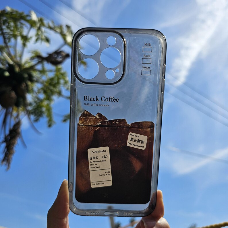 May include: Clear phone case with a black border, featuring a graphic of iced black coffee with ice cubes. The case has text that reads "Black Coffee" and "Daily coffee moments". Additional text includes "Milk", "Soda", and "Sugar".