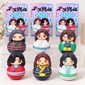 May include: Nine rounded chibi-style figurines featuring various characters with distinct hair colours and outfits, arranged in three rows. Behind them are three identical product boxes with Chinese text and illustrations of the characters.