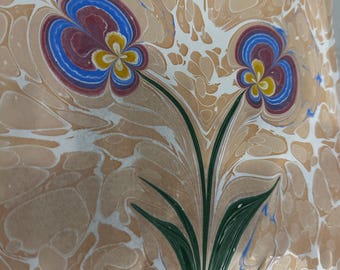 May include: A marbled paper background with a stylized green plant with two flowers. The flowers are blue, red, and yellow.