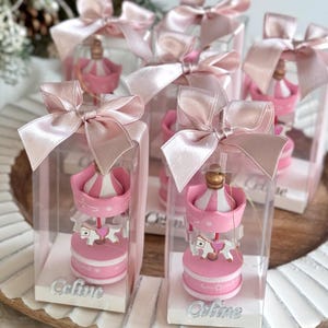 Pink carousel party favors in clear gift boxes with satin ribbons and personalized acrylic names – ideal for baby showers or baptisms. Close-up of pink carousel keepsakes with gold and silver bows, featuring custom names and elegant acrylic details. Colorful carousel favors (red, blue, green, yellow) with festive ribbons, designed as personalized welcome baby or birthday gifts.