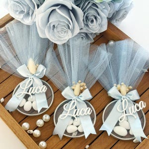 Personalized blue baptism favor with almond candies, custom name ‘Luca’ on acrylic tag, wrapped in soft blue tulle with satin ribbon and dried flowers – elegant handmade bomboniere for baby boy christening or baby shower