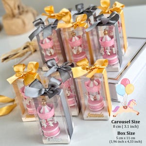 Pink carousel party favors in clear gift boxes with satin ribbons and personalized acrylic names – ideal for baby showers or baptisms. Close-up of pink carousel keepsakes with gold and silver bows, featuring custom names and elegant acrylic details. Colorful carousel favors (red, blue, green, yellow) with festive ribbons, designed as personalized welcome baby or birthday gifts.