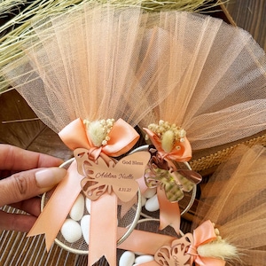 Peach tulle baptism favor with butterfly acrylic tag engraved with baby name and date, satin ribbon, dried flower detail, and white almond candies – handmade personalized bomboniere gift for christening or baptism