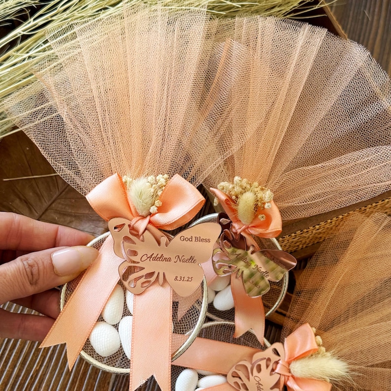 Peach tulle baptism favor with butterfly acrylic tag engraved with baby name and date, satin ribbon, dried flower detail, and white almond candies – handmade personalized bomboniere gift for christening or baptism