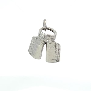 Op de afbeelding: Een zilverkleurige bedel in de vorm van een paar cowboylaarzen. De laarzen hebben gedetailleerde stiksels en een lus om aan een ketting of armband te bevestigen. De bedel is waarschijnlijk van metaal en is ontworpen als hanger.