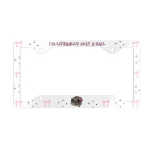 Può includere: Un telaio per targa bianco con un motivo a fiocco rosa e stella. Il telaio ha uno sfondo bianco con fiocchi rosa e stelle. Il testo "I'M LITERALLY JUST A GIRL" è stampato in viola nella parte superiore del telaio. Una piccola immagine di un criceto con un fiore rosa sulla testa è al centro del telaio.