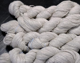 Può includere: Primo piano di diversi gomitoli di filato grigio chiaro. Il filato è avvolto strettamente in fasci ordinati, con un aspetto leggermente strutturato. Il filato è legato con uno spago azzurro. Ideale per progetti di maglia e uncinetto.