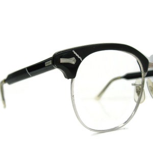 May include: Black plastic framed glasses with silver metal rims. The glasses have a cat-eye shape and a silver metal accent on the top of the frame.