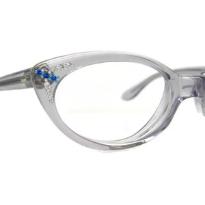 Puede incluir: Gafas grises de ojo de gato con lentes transparentes y un adorno de pedrería azul y plata en la montura izquierda.