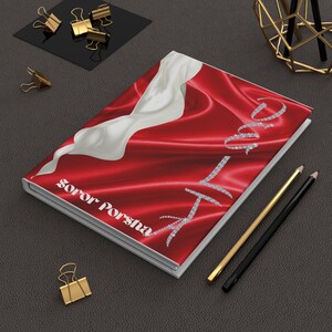 May include: A hardcover journal with a red satin cover and a white abstract design. The journal features the text "Love" in a diamond-like font and the name "Soror Porsha". Gold and black pencils and gold binder clips are also visible.