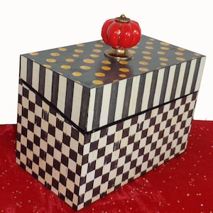 May include: A black and white checkered box with a black and white striped lid. The lid has gold polka dots and a red knob.